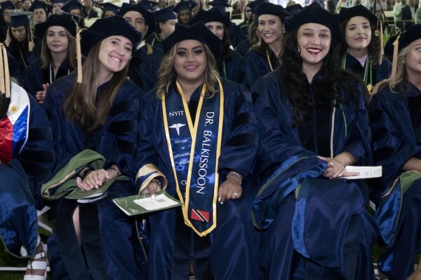 Student in blue graduation outfit sitting in crowd.