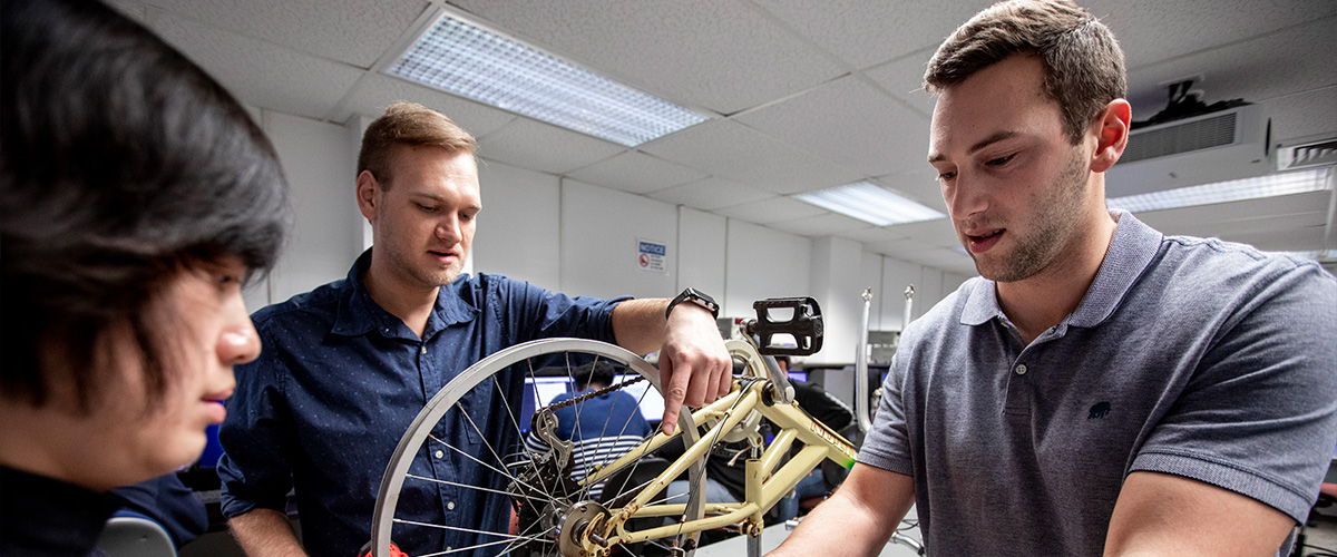 Group of three working on a bicycle in a lab.