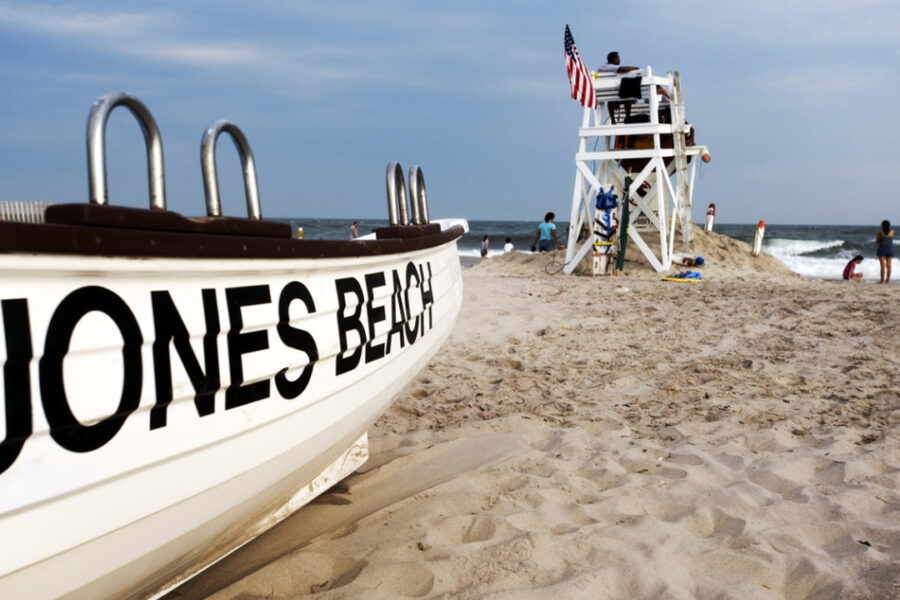 Close up of boat with "Jones Beach" on it with life guard and people in background near ocean.