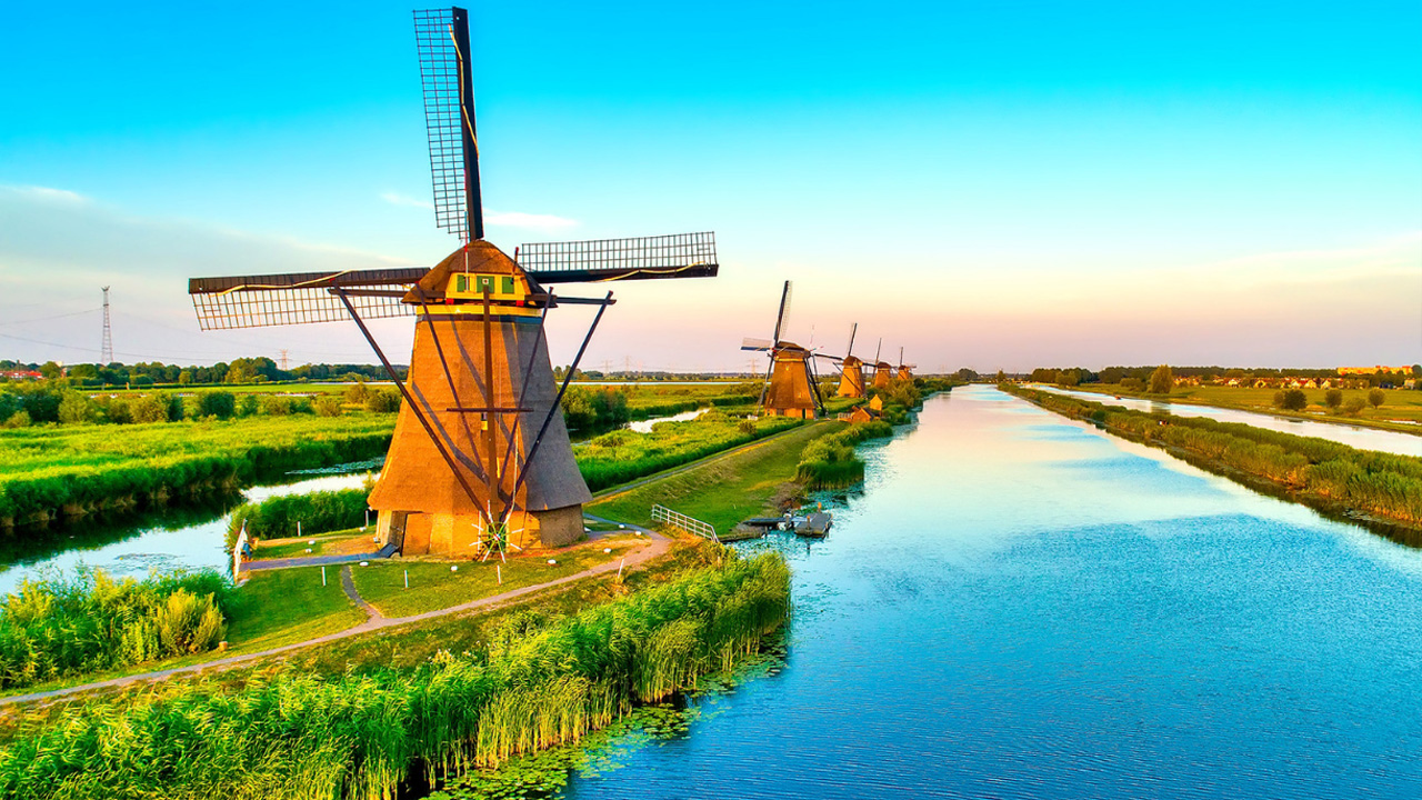 Line of windmills by a river bank.