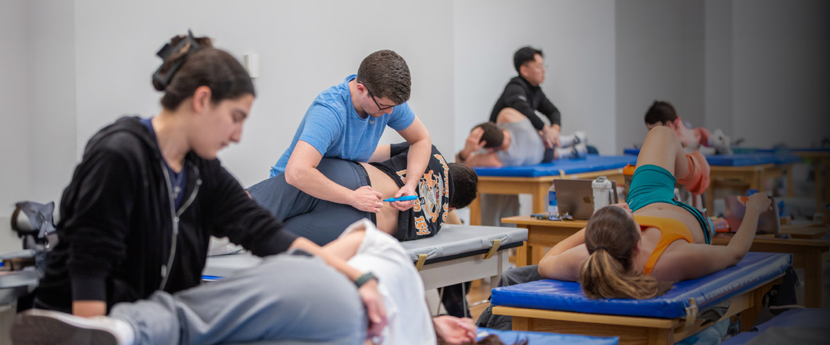 A group of students work manually on other students acting as patients to practice physical therapy techniques.