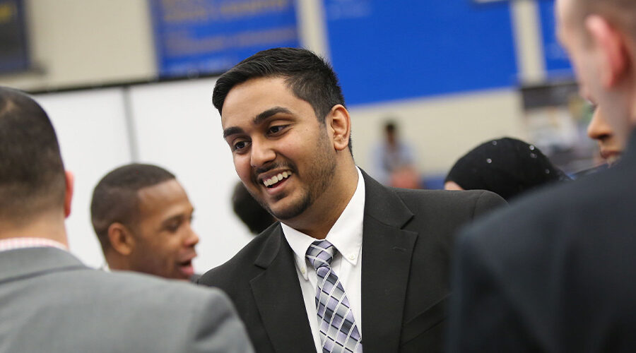 Student in suit talking to recruiters at job fair.