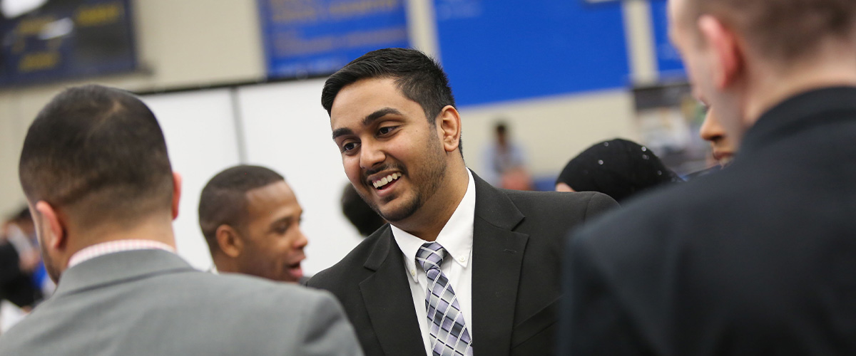 Student in suit talking to recruiters at job fair.