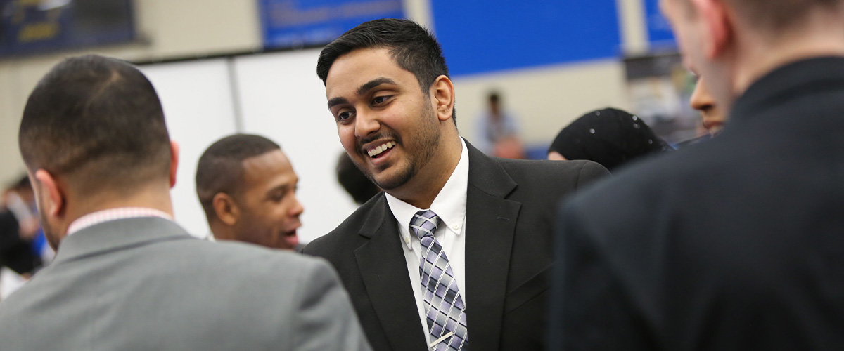 Student in suit talking to recruiters at job fair.