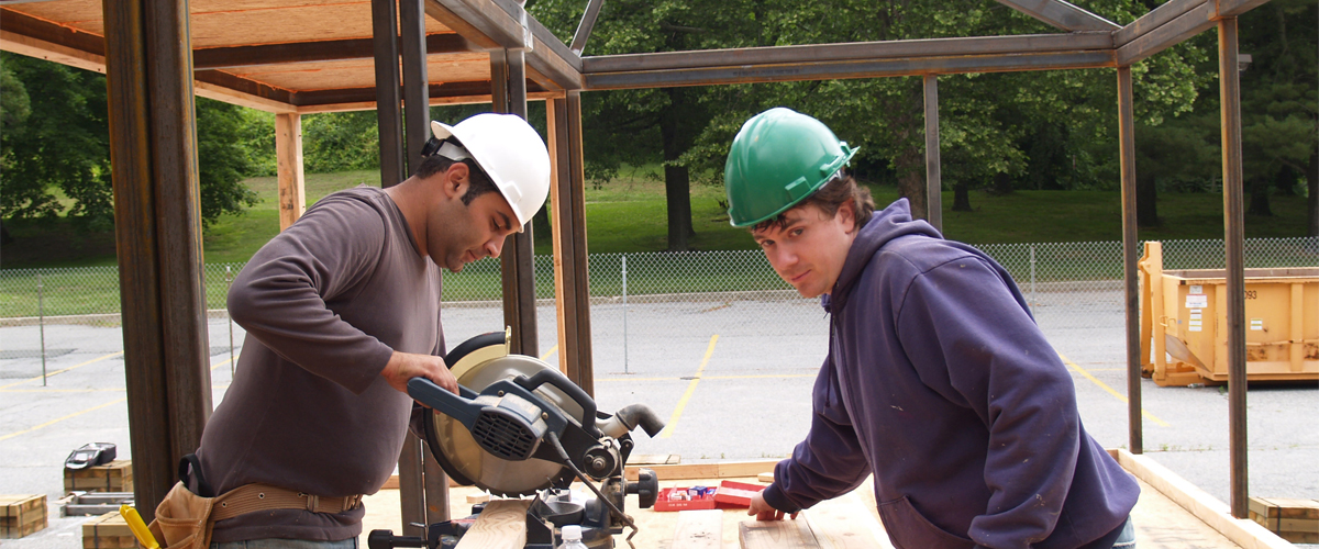 Two students work at a construction site.