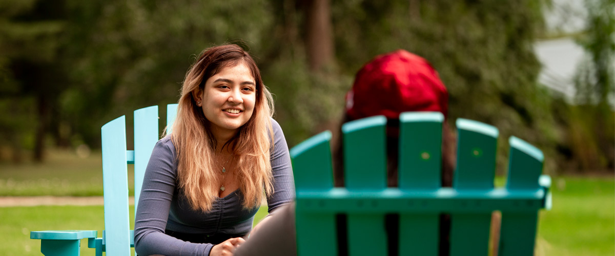 Two New York Tech students sitting outdoors in Adirondack chairs have a discussion about financial aid.