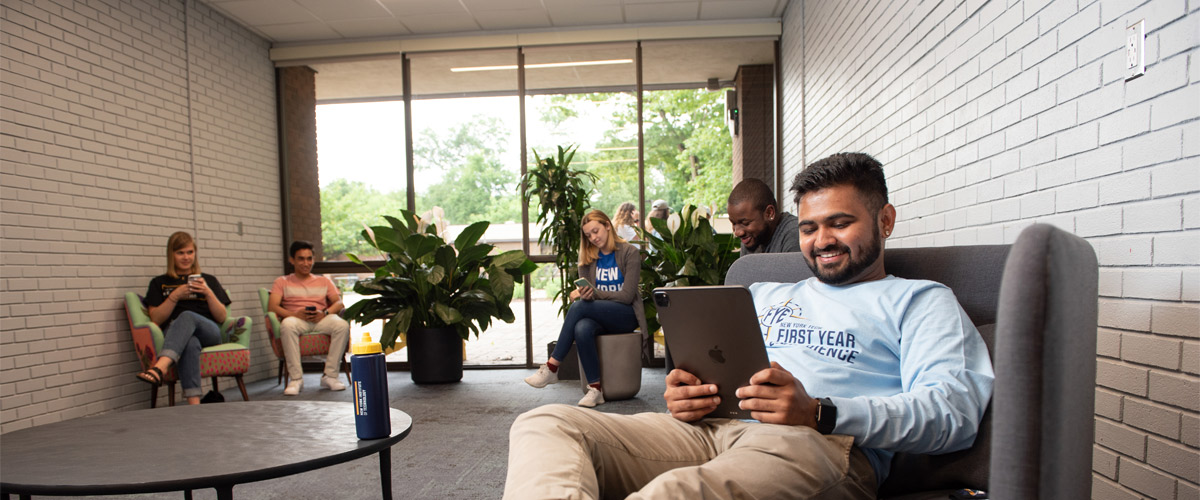 A group of first-year New York Tech students sits in a common area to review information on their smartphones or tablets.