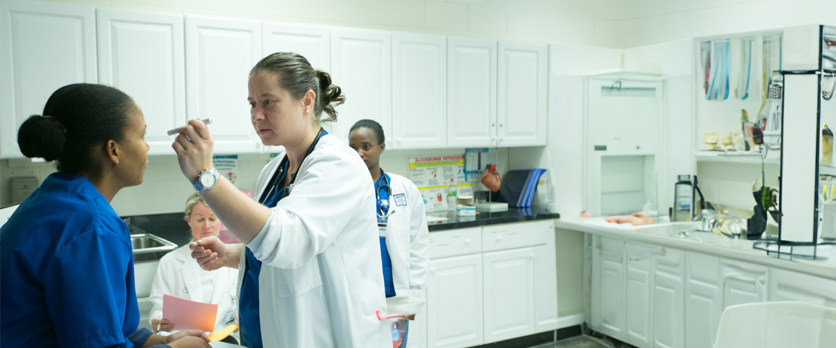 A doctor checks a patient's eyes while medical students assist.