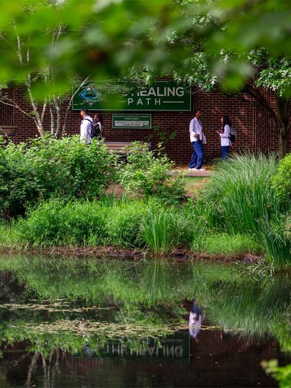 The healing path is pictured near a pond and a brick building.