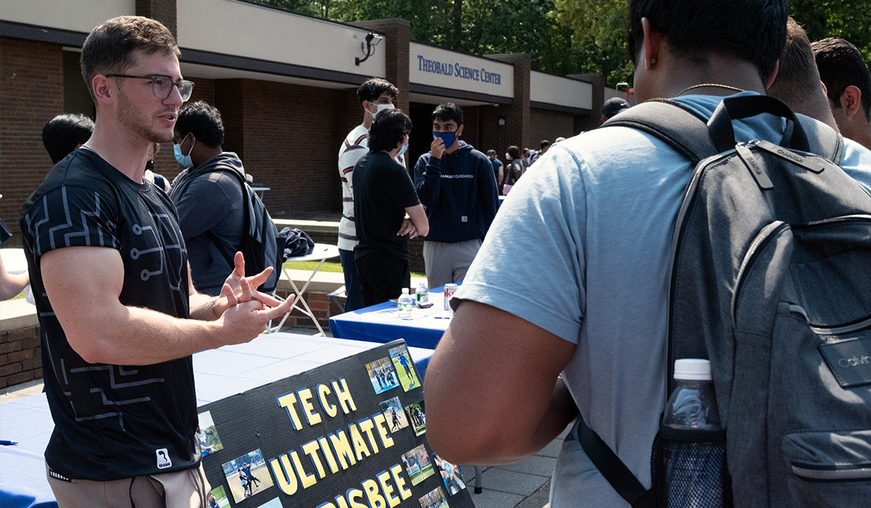 Student at booth talking to other student.