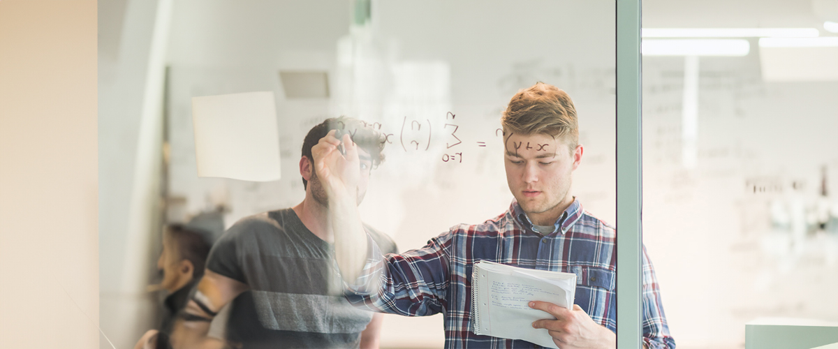 A student works on a math equation on a glass screen.