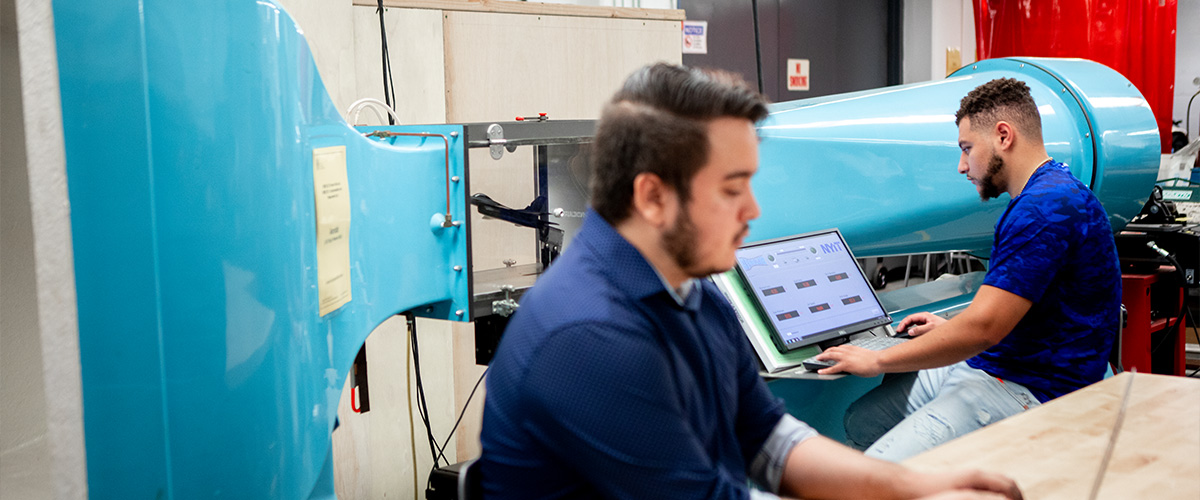 Two students working with large blue equipment and laptops.